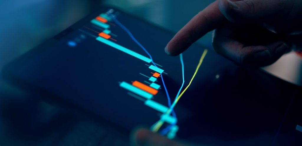 Close-up of a hand pointing at a financial trading chart on a tablet screen