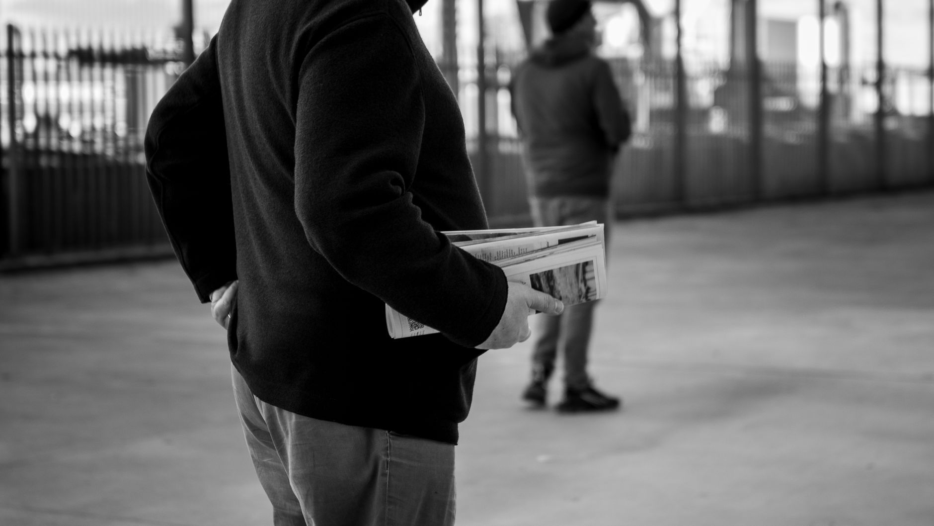 A monochrome image of a person holding newspapers in an urban environment, capturing the essence of street life. — How BDG Ga