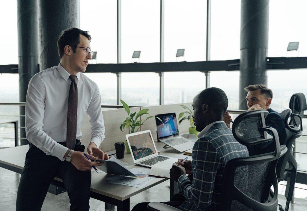 Three men engaged in a business meeting in a modern office setting with laptops and documents. — Private Investigator Melbour