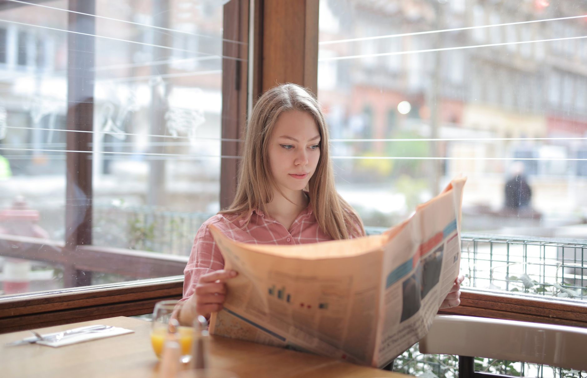 A young woman enjoying a newspaper at a cafe table, immersed in reading. — Unlocking VIP Rewards on 82 Lottery