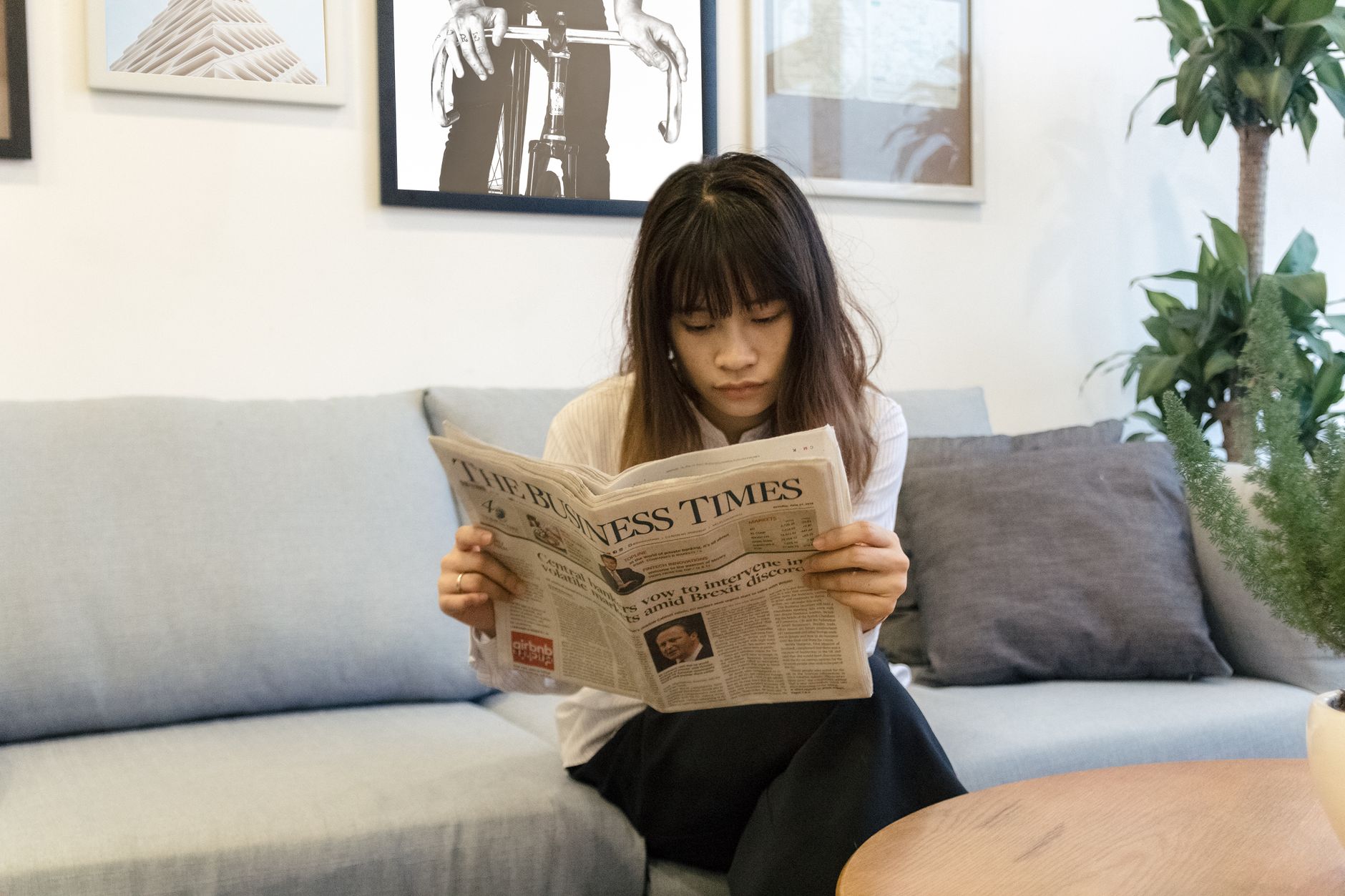 A young woman attentively reads a newspaper while sitting on a modern sofa indoors. — Why Students Love Playing on OK Win App
